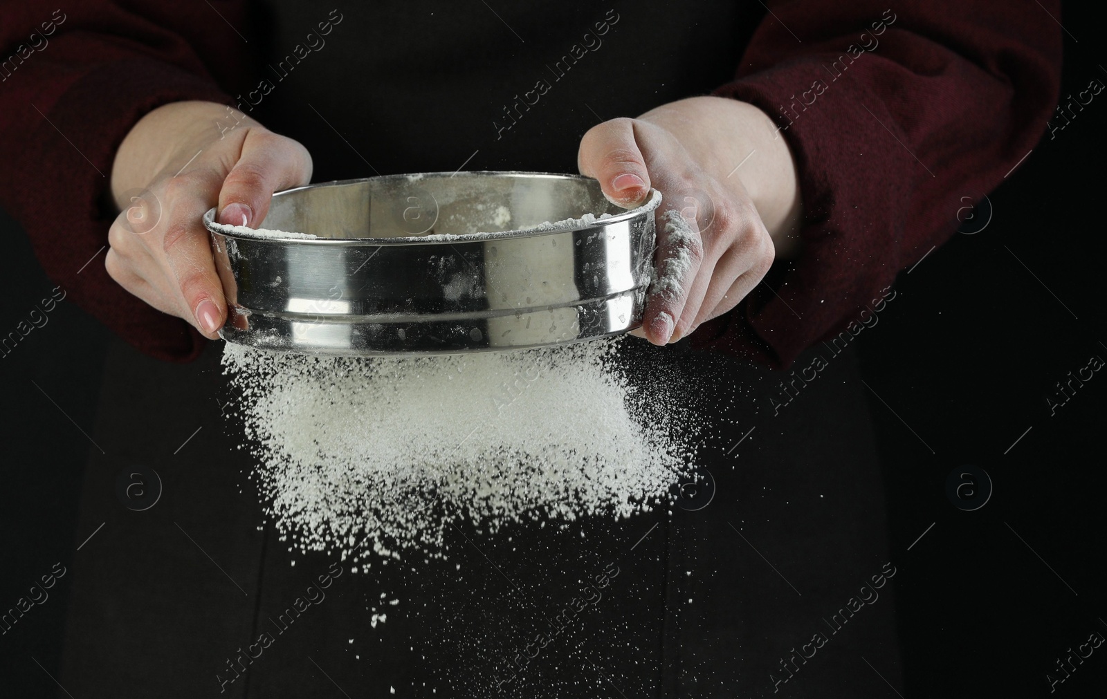 Photo of Woman sieving flour at table against black background, closeup