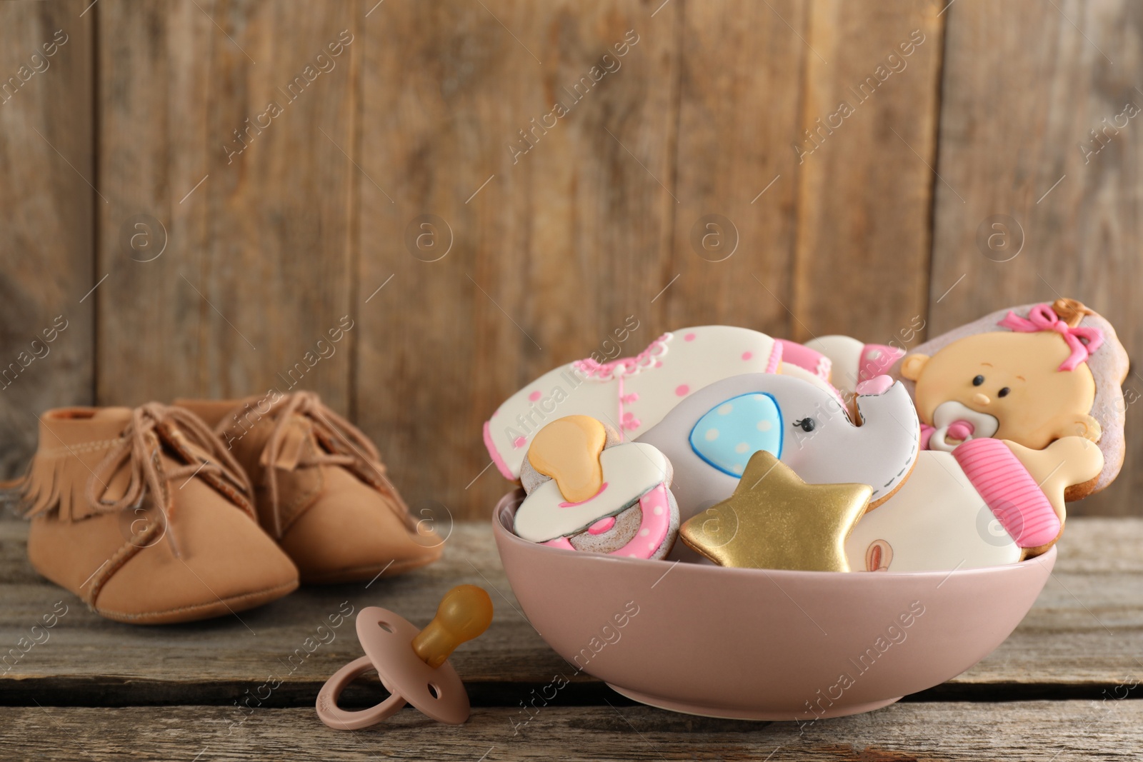 Photo of Cute tasty cookies of different shapes, pacifier and booties on wooden table. Baby shower party