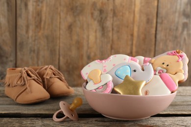 Photo of Cute tasty cookies of different shapes, pacifier and booties on wooden table. Baby shower party