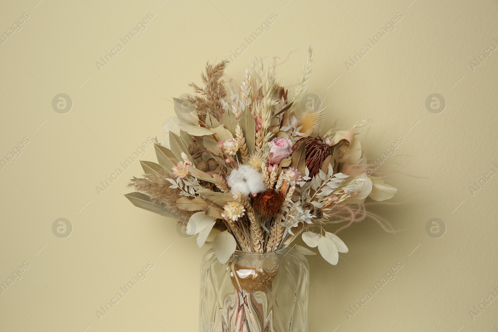 Photo of Beautiful dried flower bouquet in glass vase against beige background