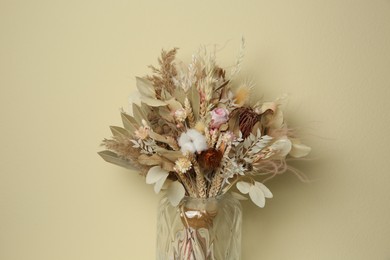 Beautiful dried flower bouquet in glass vase against beige background