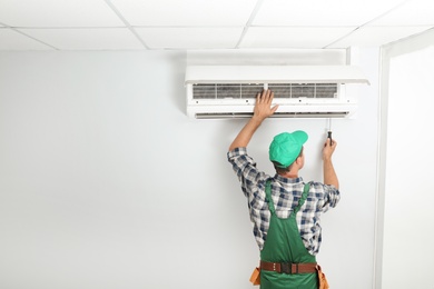 Photo of Male technician fixing modern air conditioner indoors