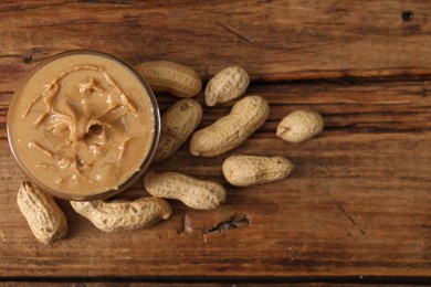 Delicious nut butter in bowl and peanuts on wooden table, top view