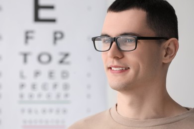 Photo of Young man with glasses against vision test chart