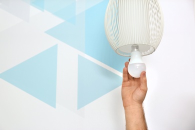 Man changing light bulb in lamp against color wall, closeup. Space for text