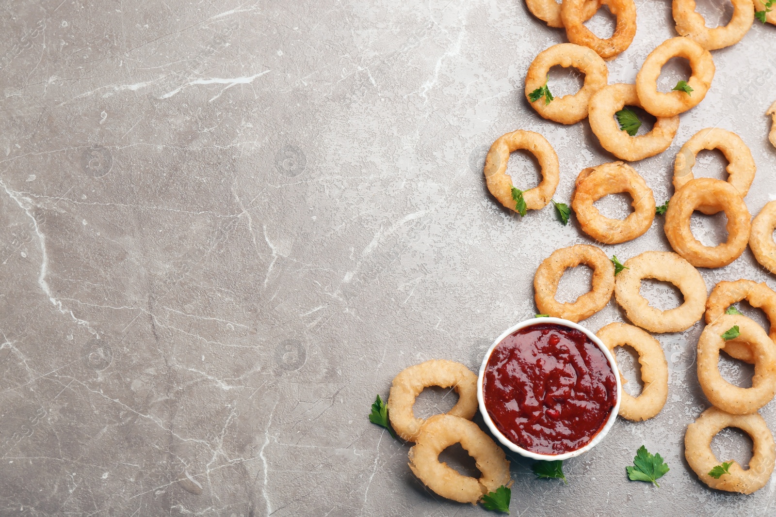 Photo of Fried onion rings and bowl of sauce on grey background, top view