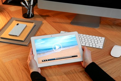 Woman watching video on tablet at wooden desk, closeup