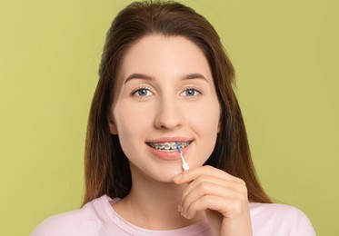 Photo of Smiling woman with dental braces cleaning teeth using interdental brush on light green background