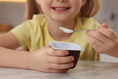 Cute little girl with tasty yogurt at white marble table indoors, closeup