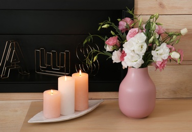 Burning candles and vase with flowers on table against wooden wall