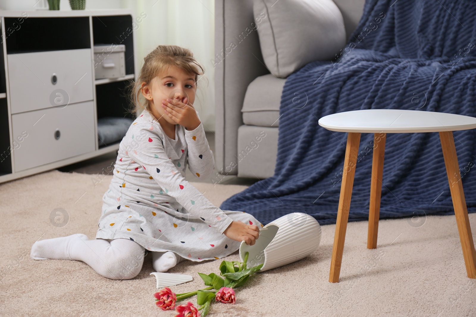 Photo of Emotional little girl and broken ceramic vase on floor at home
