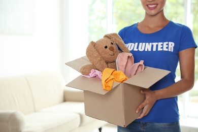 Photo of Female volunteer holding box with donations indoors. Space for text