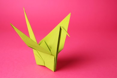 Photo of Origami art. Handmade paper crane on pink background, closeup. Space for text