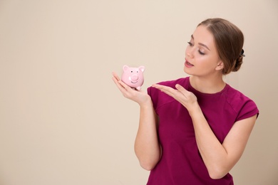 Young woman with piggy bank and space for text on color background. Money saving