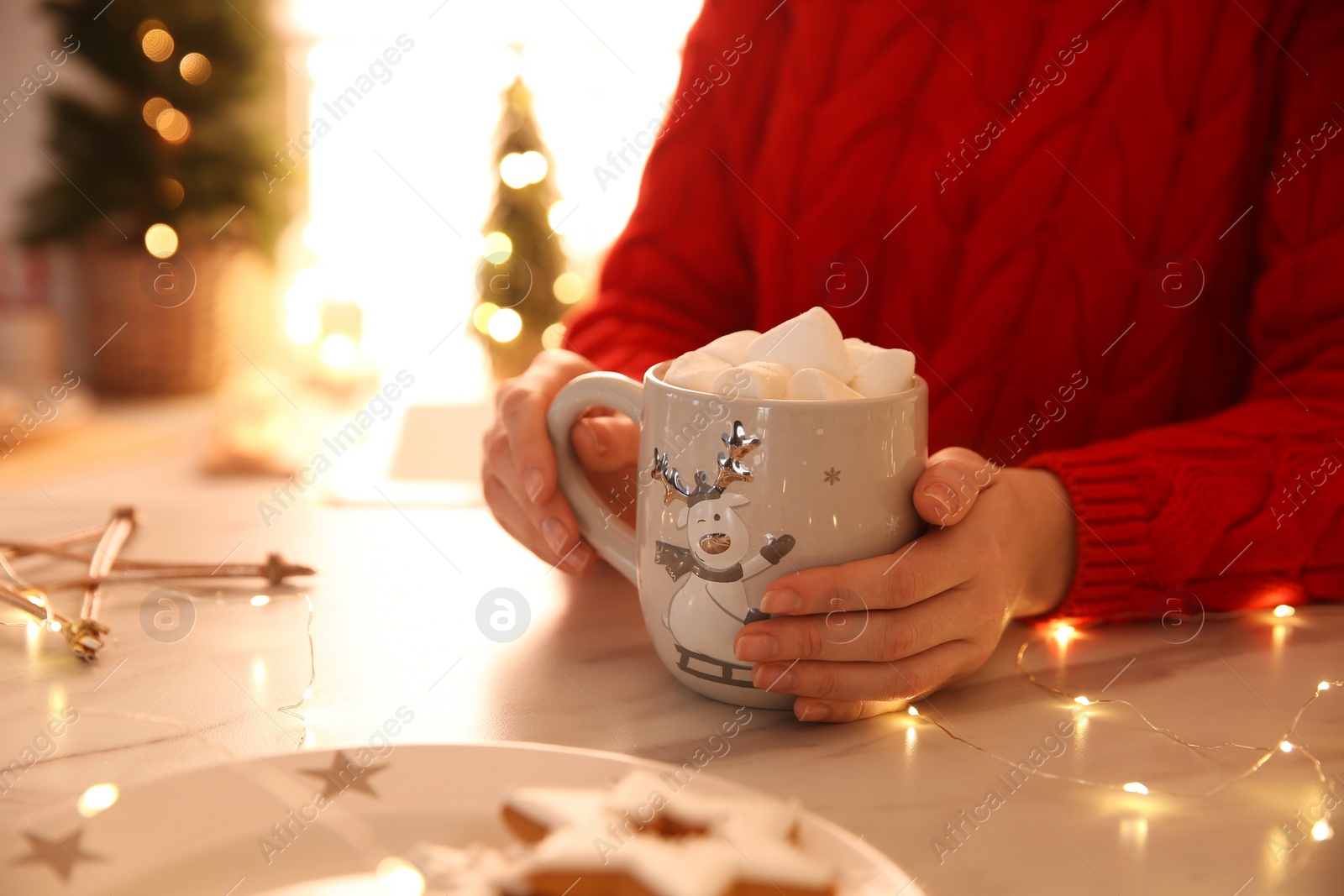 Photo of Woman holding cup of hot drink with marshmallow indoors, closeup