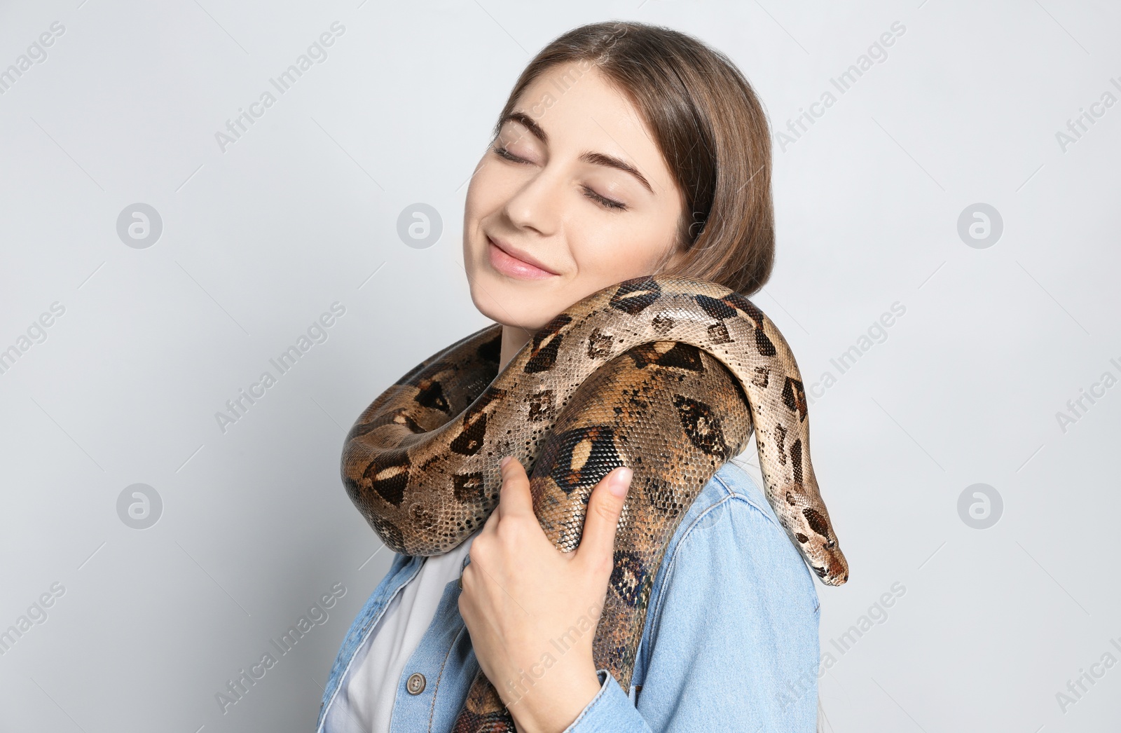 Photo of Young woman with boa constrictor on light background. Exotic pet