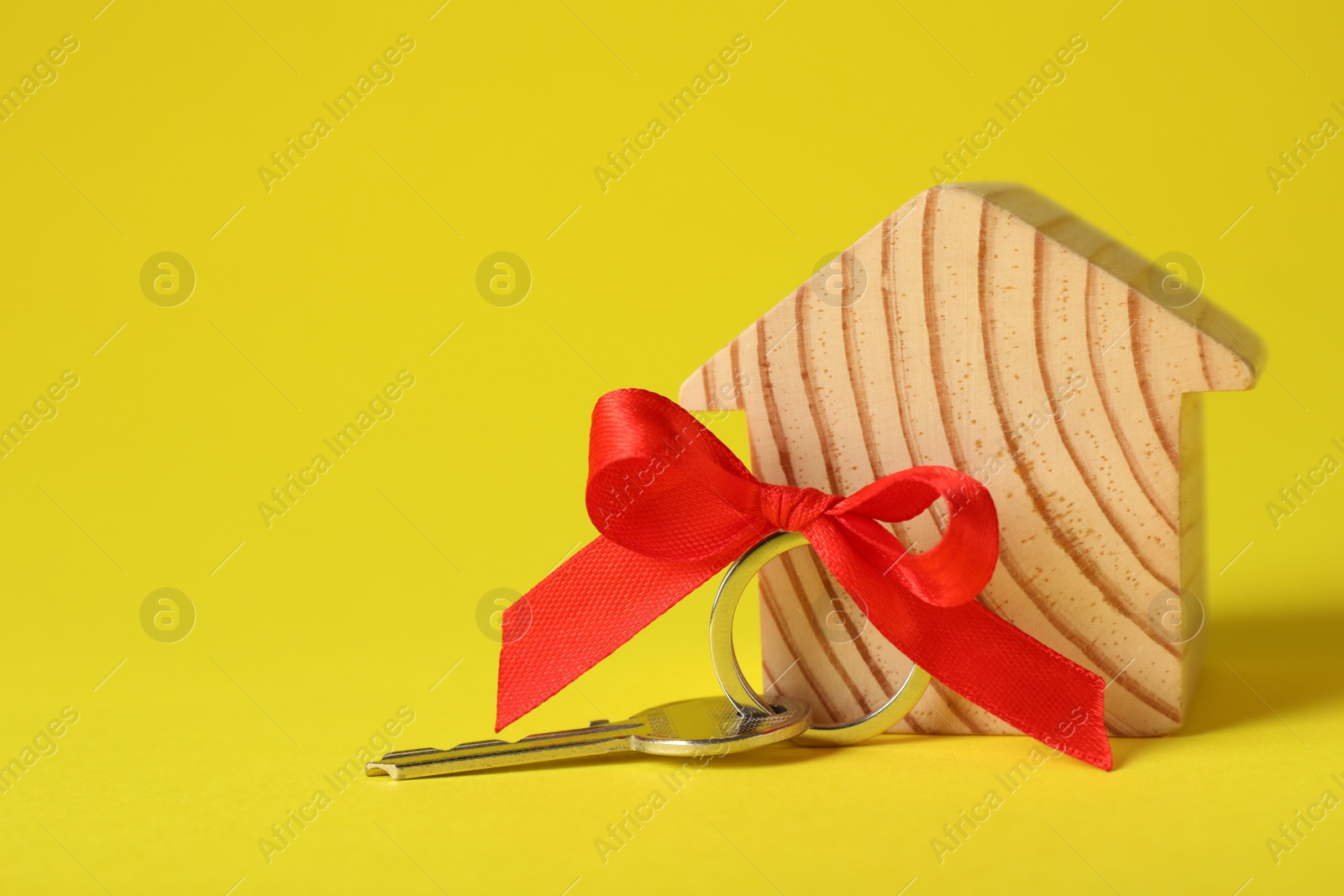 Photo of Wooden house model with red bow and key on yellow background, space for text. Housewarming party