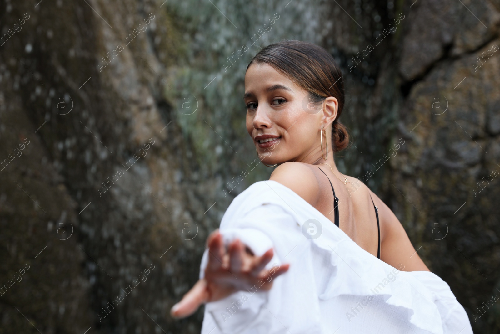 Photo of Beautiful young woman near waterfall outdoors, space for text