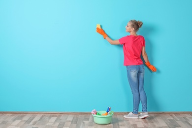 Photo of Woman in gloves cleaning color wall with rag