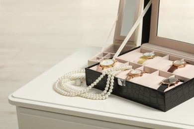 Jewelry boxes with many stylish wristwatches and pearl necklace on white table. Space for text