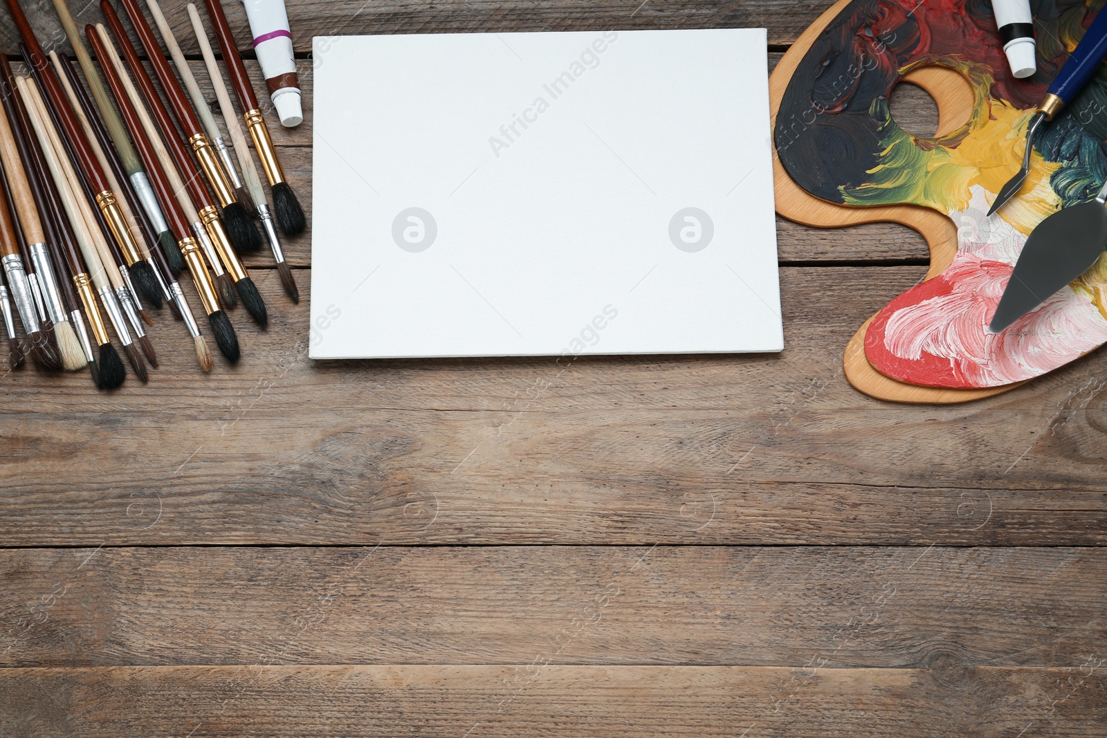 Photo of Blank canvas, brushes, palettes and paints on wooden table, flat lay. Space for text