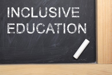 Image of Phrase INCLUSIVE EDUCATION and piece of white chalk on blackboard, top view
