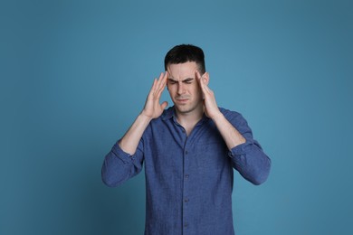 Photo of Young man suffering from headache on blue background, space for text. Cold symptoms