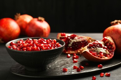 Photo of Tasty ripe pomegranates and grains on dark wooden table