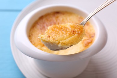Photo of Taking delicious creme brulee with spoon from bowl at light blue table, closeup