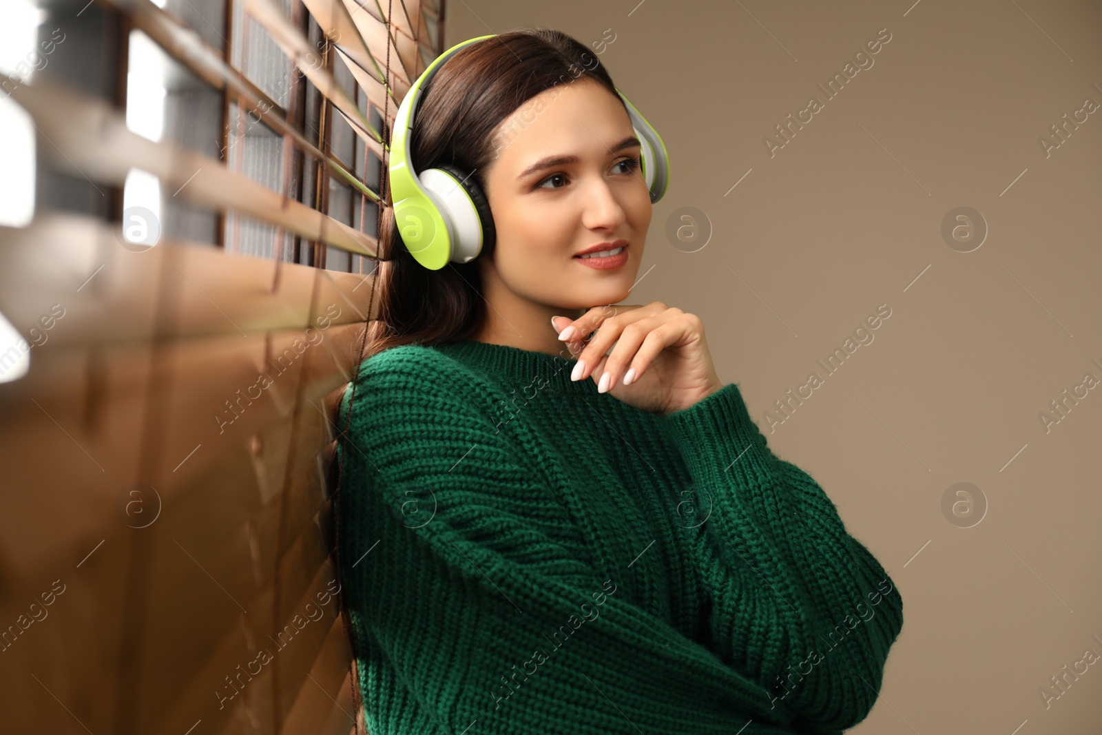 Photo of Young woman listening to audiobook near window indoors