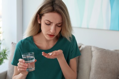 Upset young woman with abortion pill and glass of water at home