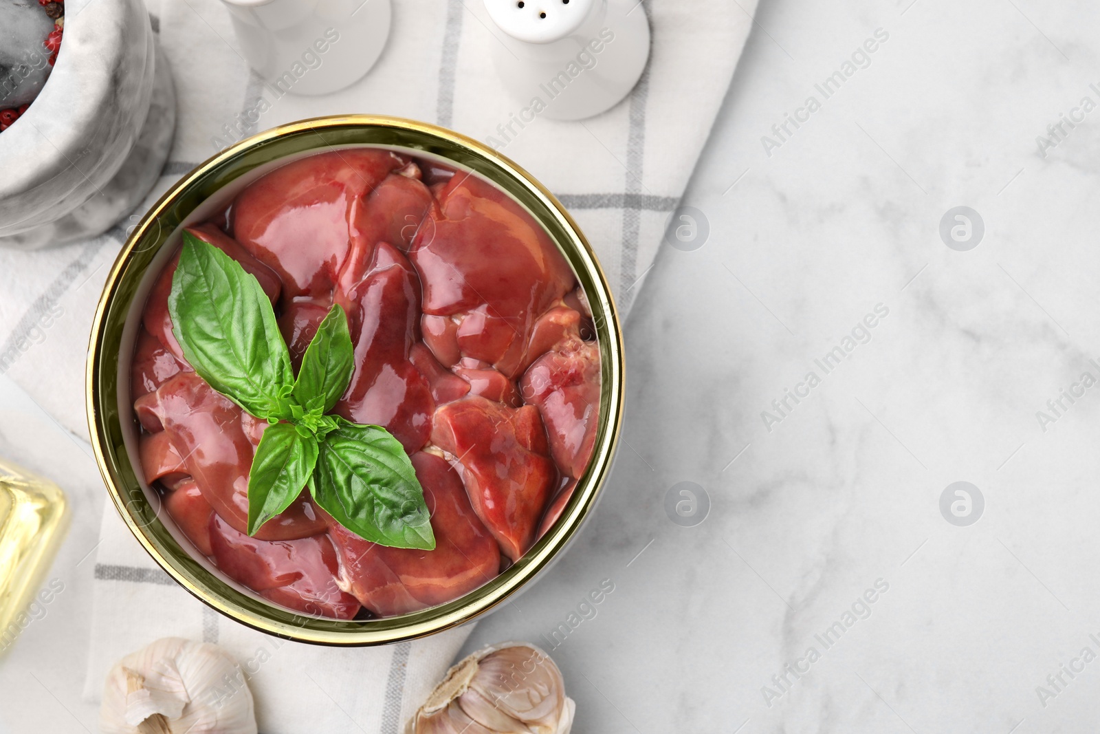 Photo of Bowl with raw chicken liver, basil and garlic on white marble table, flat lay. Space for text