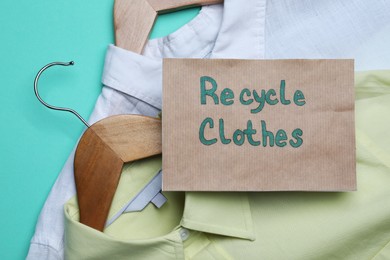 Photo of Recycling concept. Clothes and card with phrase on turquoise background, closeup