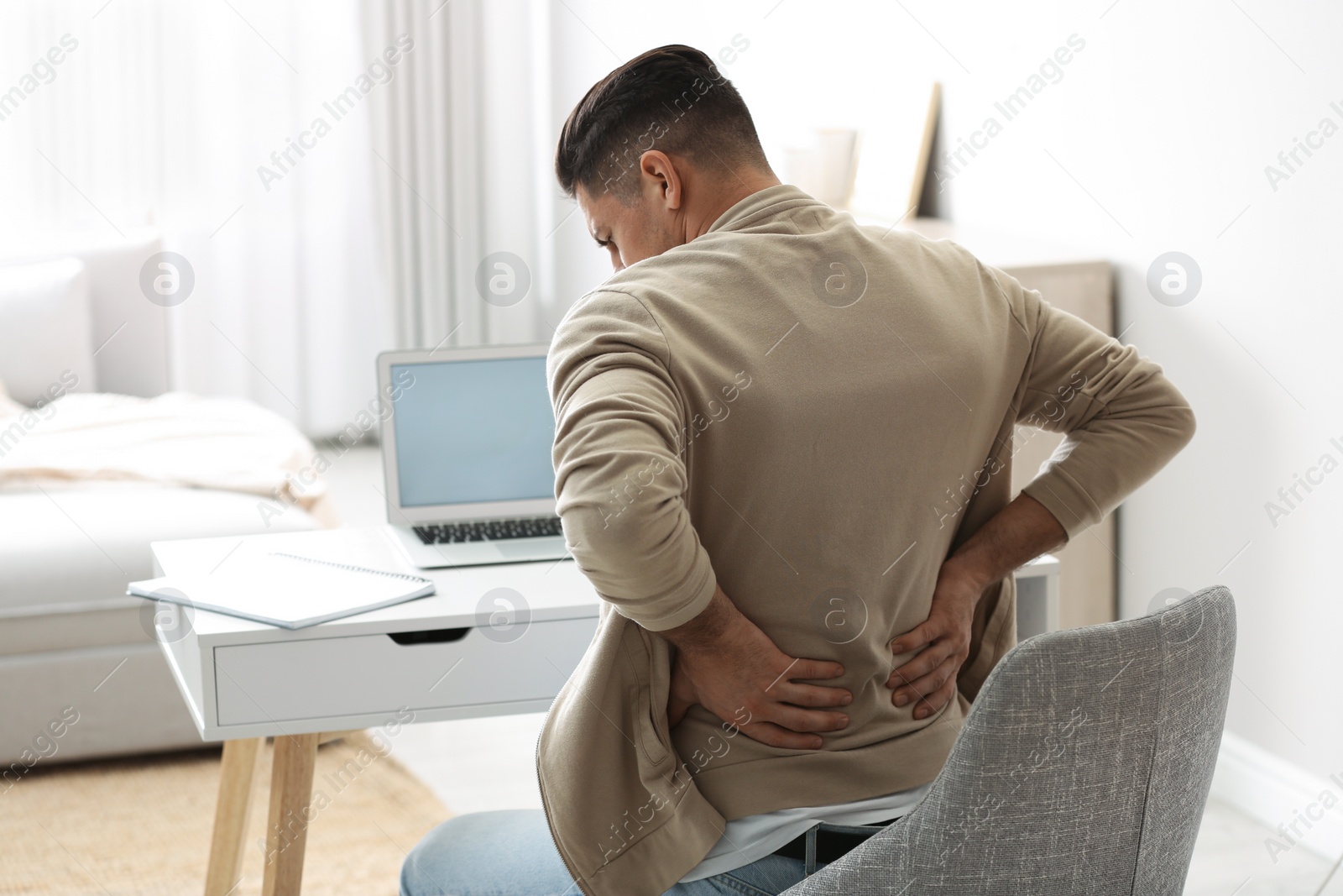 Photo of Man suffering from back pain at workplace. Bad posture problem