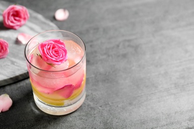 Photo of Glass of refreshing drink with lemon and roses on grey table. Space for text