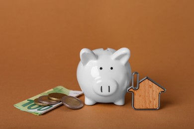 Ceramic piggy bank, money and key trinket on brown background. Financial savings