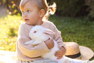 Photo of Cute little girl with adorable rabbit outdoors on sunny day