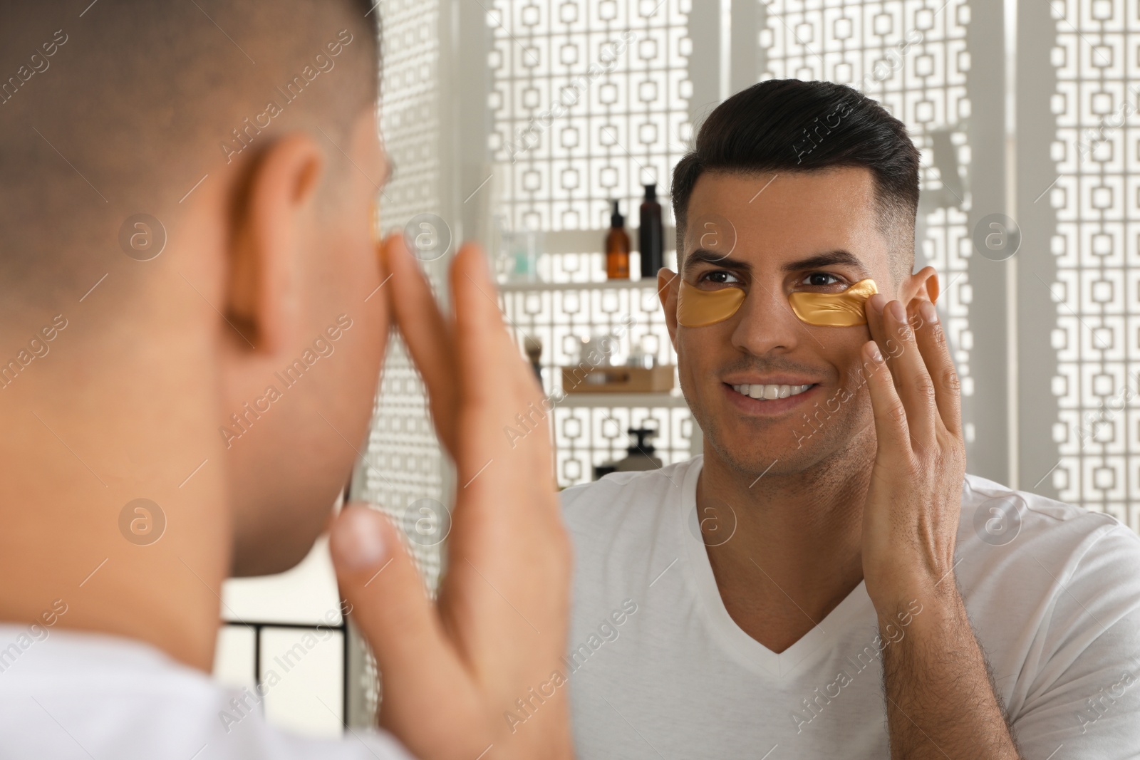 Photo of Man applying golden under eye patch near mirror at home