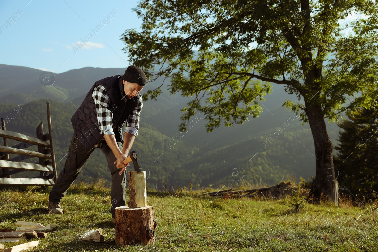 Photo of Handsome man with axe cutting firewood in mountains