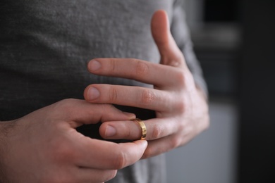 Photo of Man taking off wedding ring on blurred background, closeup. Divorce concept