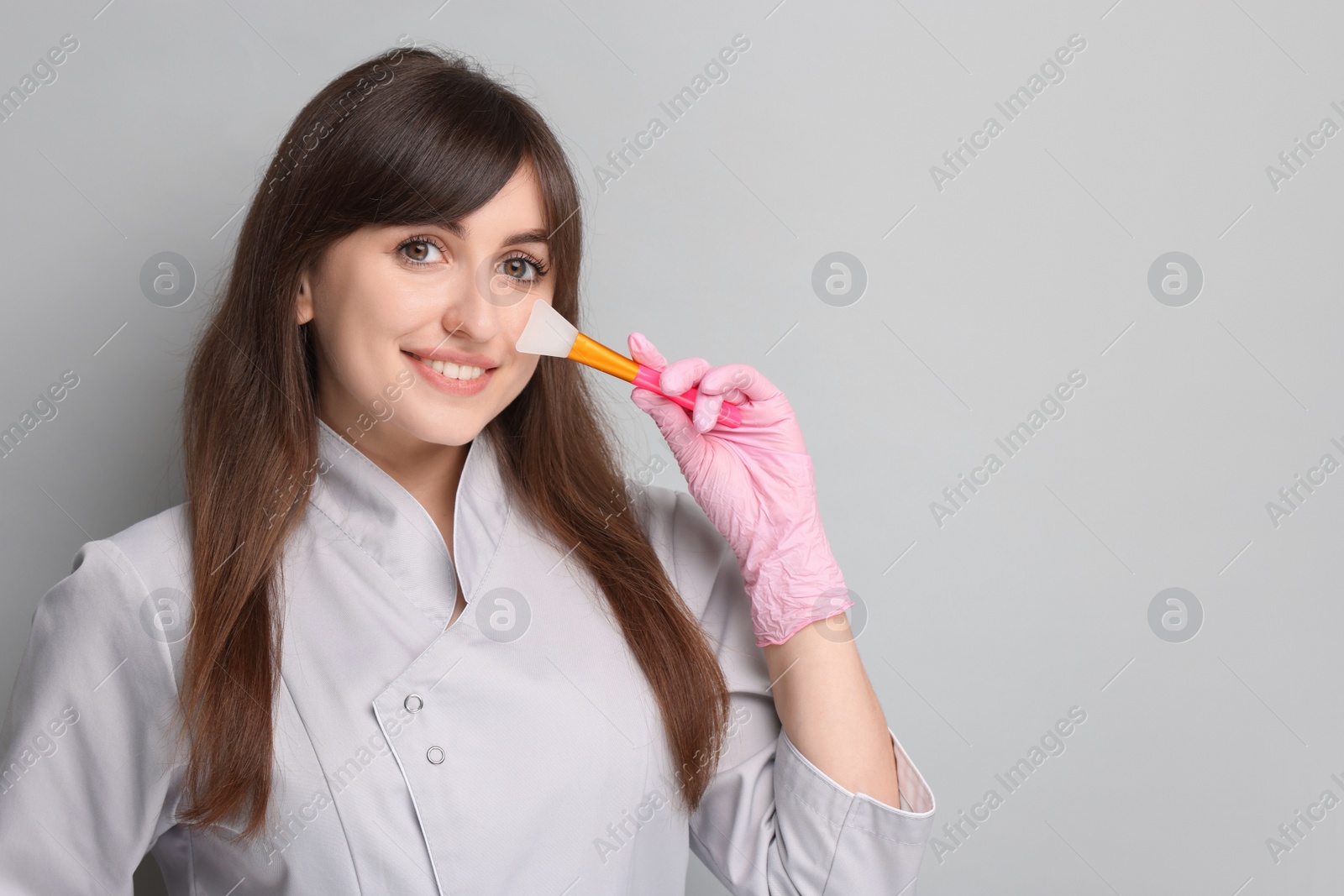 Photo of Cosmetologist with silicone cosmetic brush on grey background, space for text