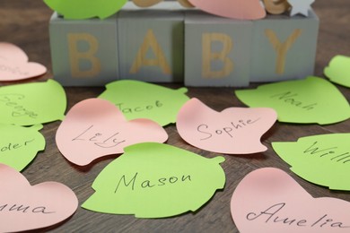 Photo of Cubes with word Baby and paper stickers with different names on wooden table, closeup. Choosing baby's name