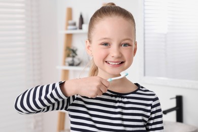 Photo of Cute little girl brushing her teeth with plastic toothbrush in bathroom