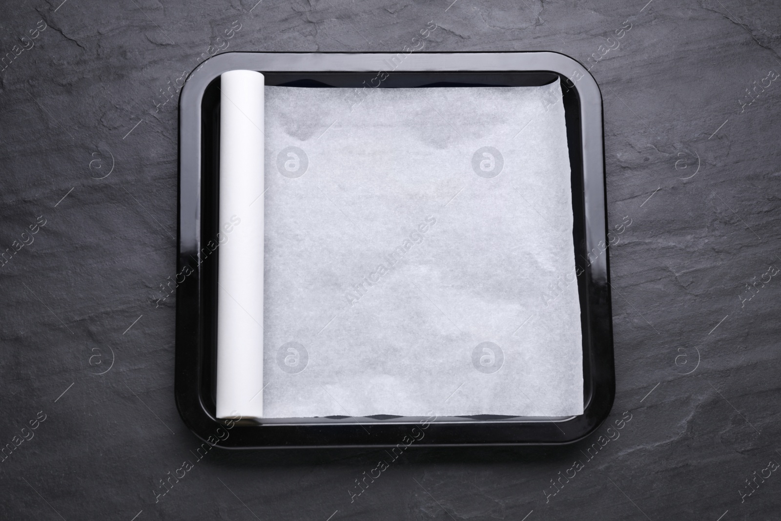 Photo of Baking pan with parchment paper on black slate background, top view