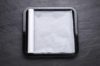 Photo of Baking pan with parchment paper on black slate background, top view