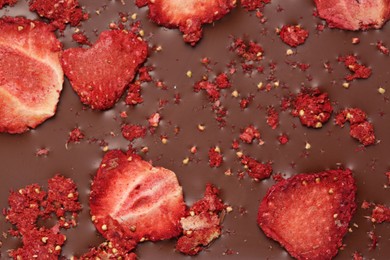 Photo of Chocolate bar with freeze dried strawberries as background, closeup