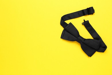Photo of Stylish black bow tie on yellow background, top view. Space for text