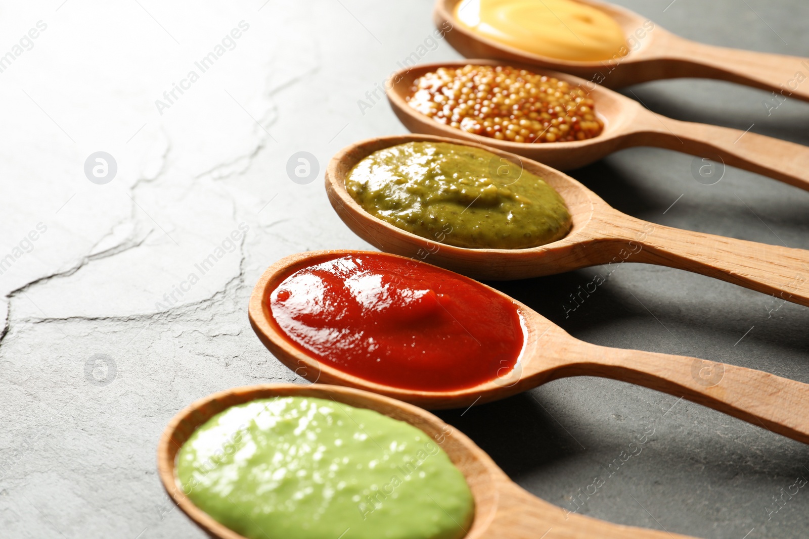 Photo of Set of wooden spoons with different delicious sauces on grey table, closeup