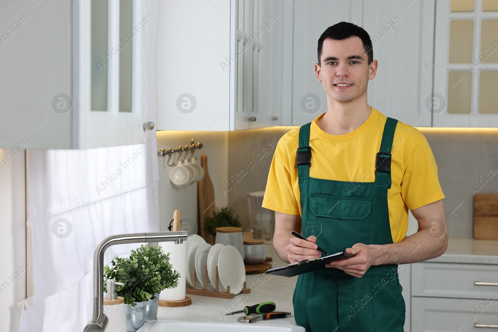 Photo of Smiling plumber with clipboard near faucet in kitchen