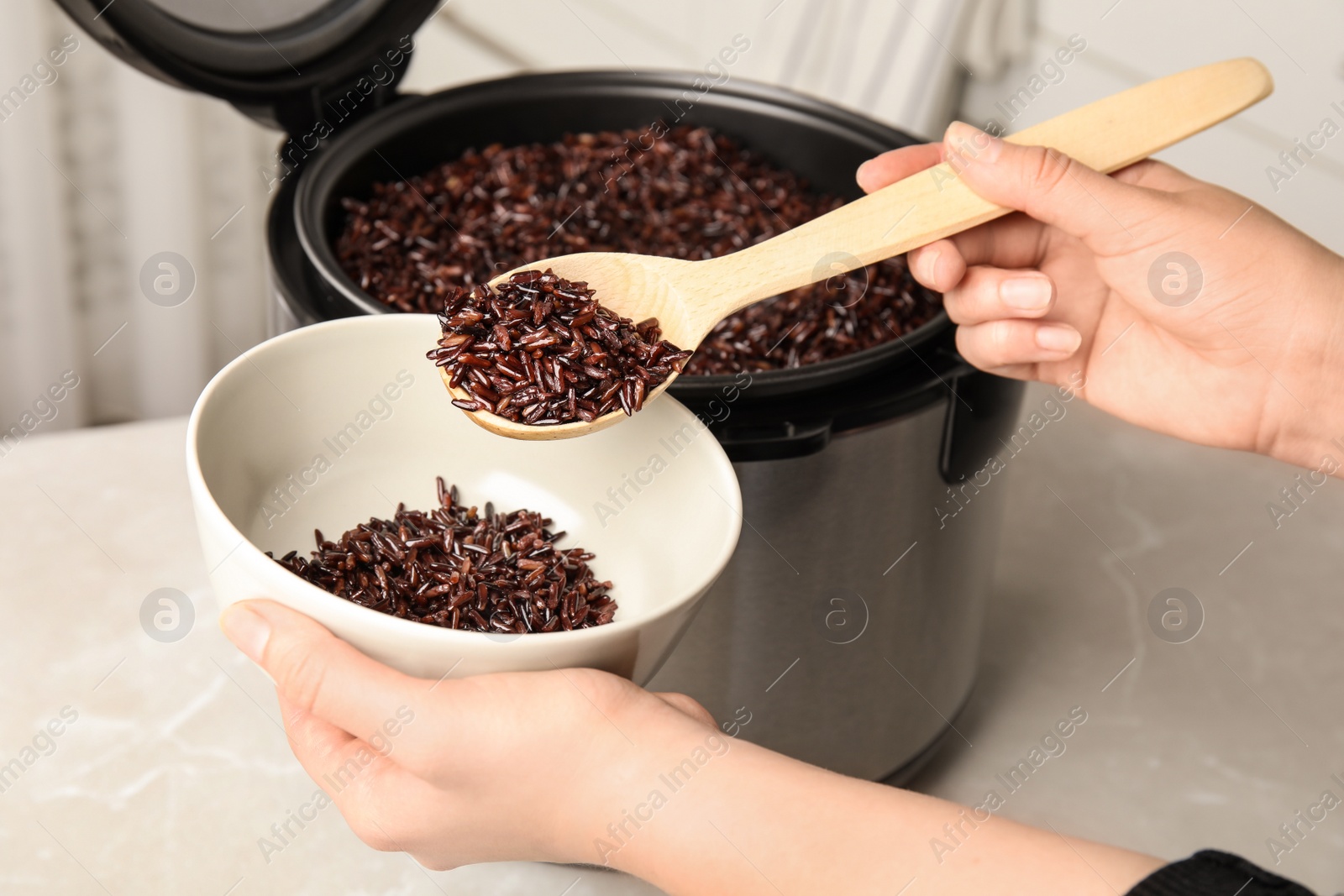 Photo of Woman putting delicious brown rice into bowl from multi cooker, closeup